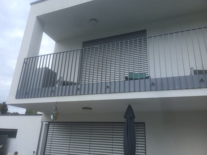 Balkon mit grauem Stabgeländer an einer modernen weißen Hausfassade.