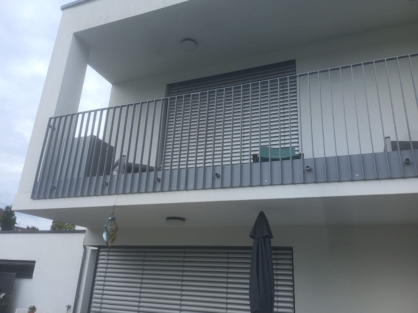 Balkon mit grauem Stabgeländer an einer modernen weißen Hausfassade.
