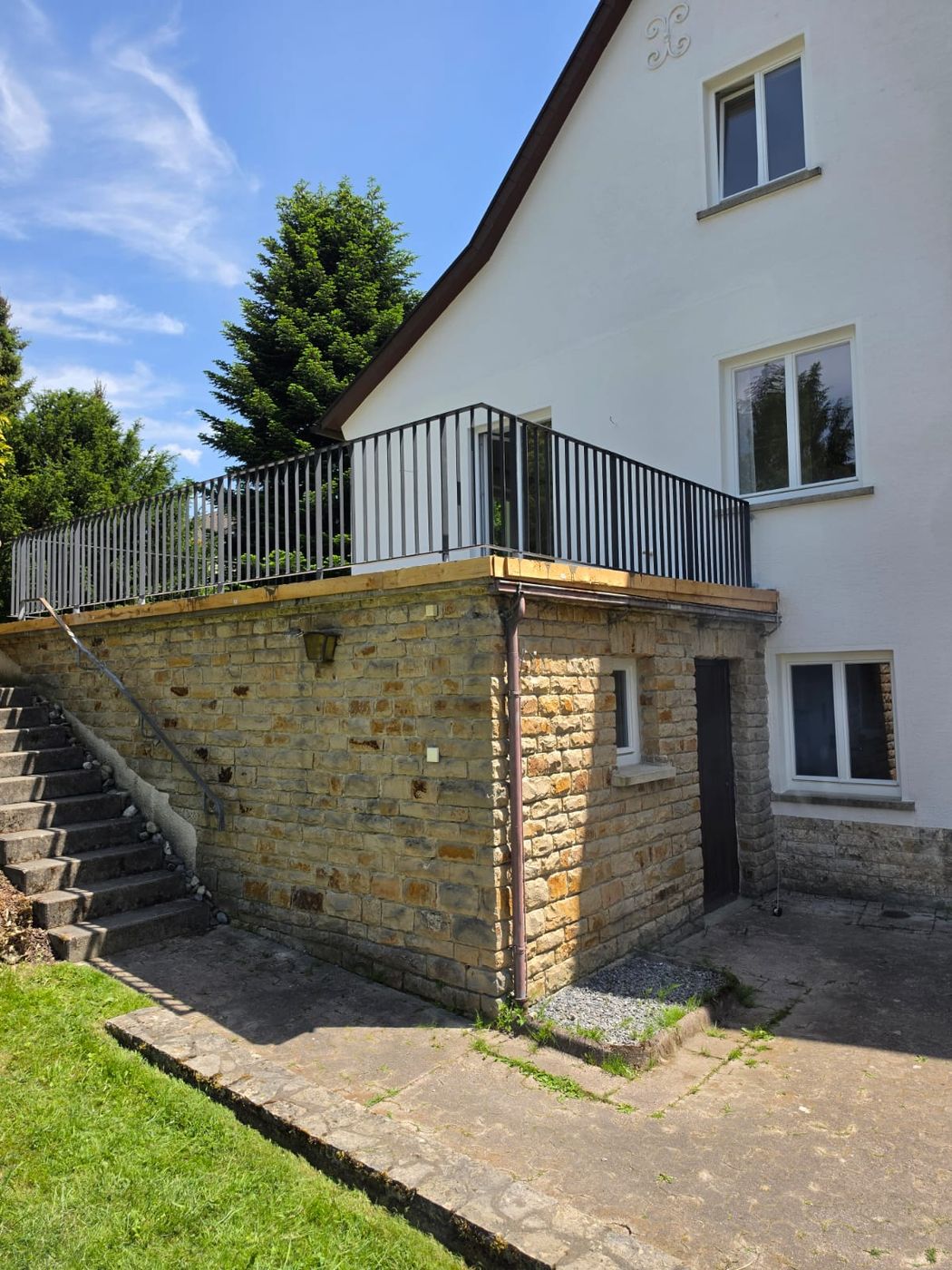 Erhöhte Terrasse auf Natursteinunterbau mit Metallgeländer an einem Wohnhaus.