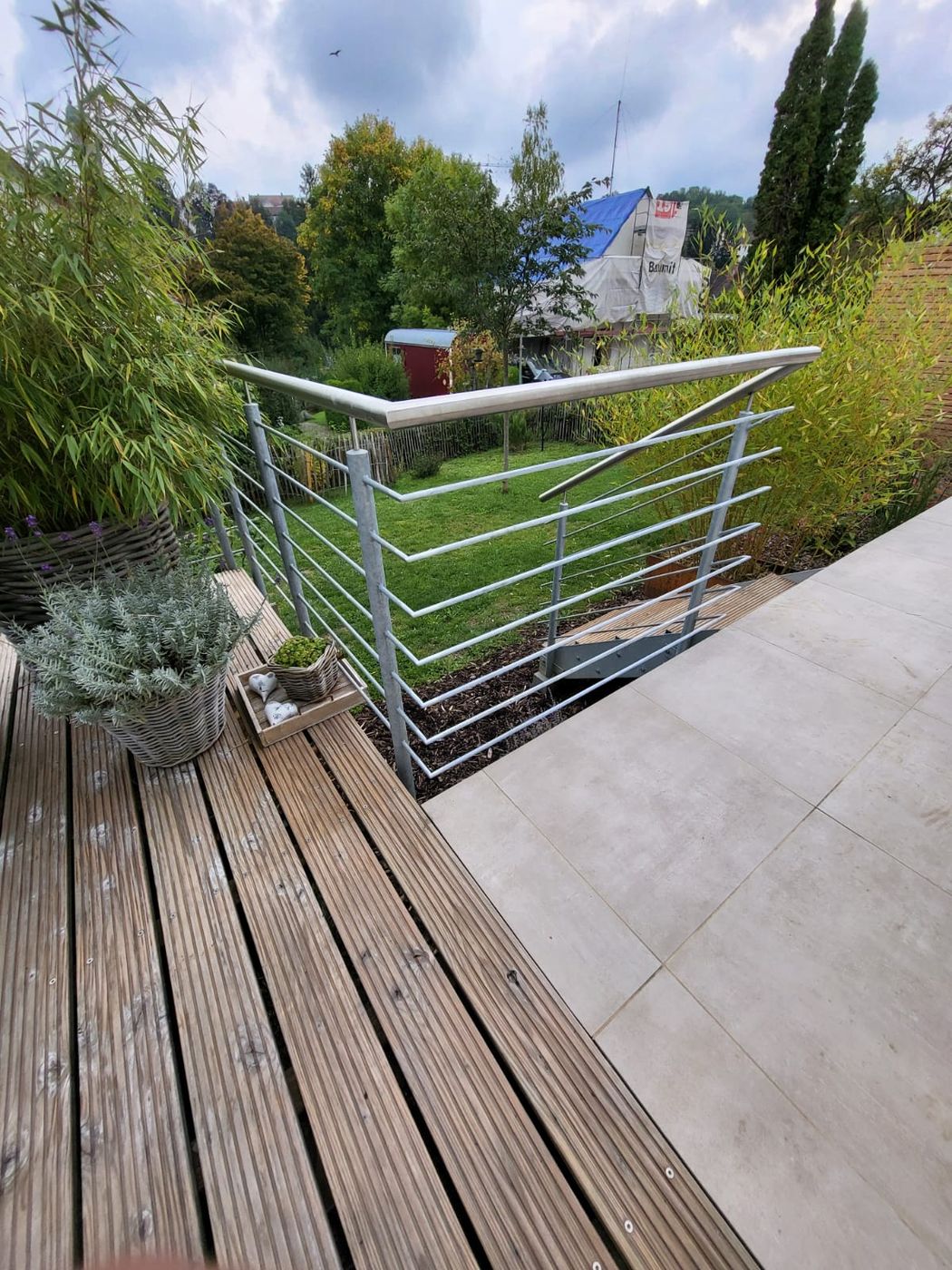 Ecke eines Metallgeländers mit waagerechten Streben an einer Holzterrasse.