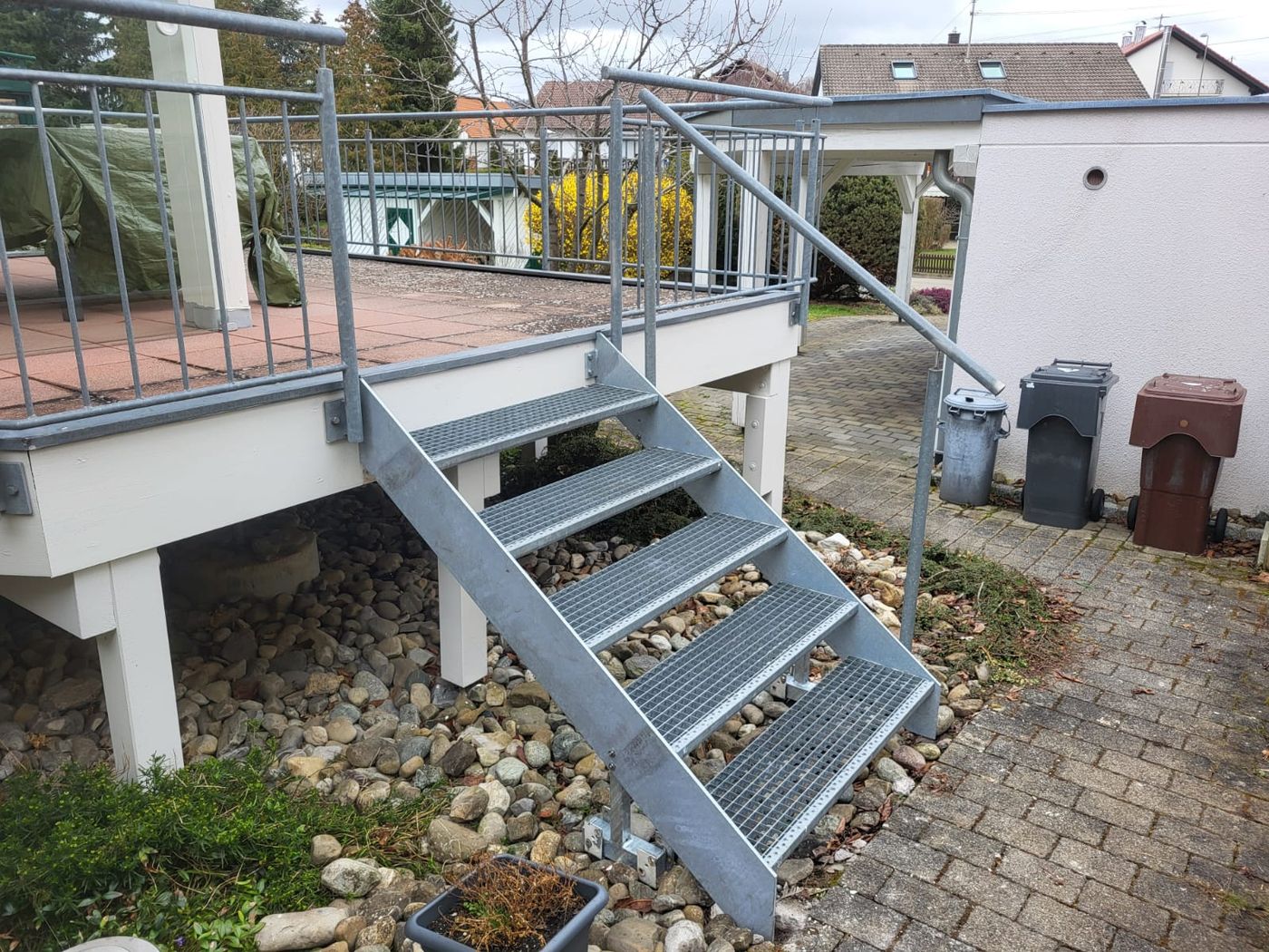 Seitliche Ansicht einer kurzen Gitterrosttreppe zwischen Terrasse und Garten.