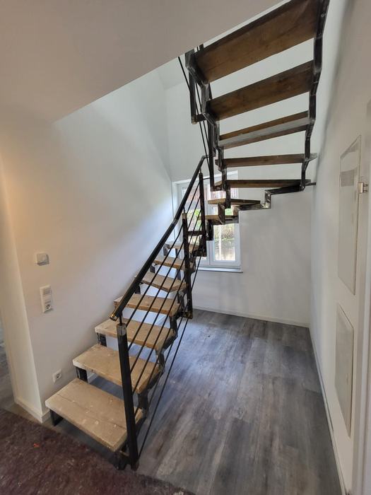 Offene gewendelte Holztreppe mit schwarzer Metallkonstruktion und Geländer.
