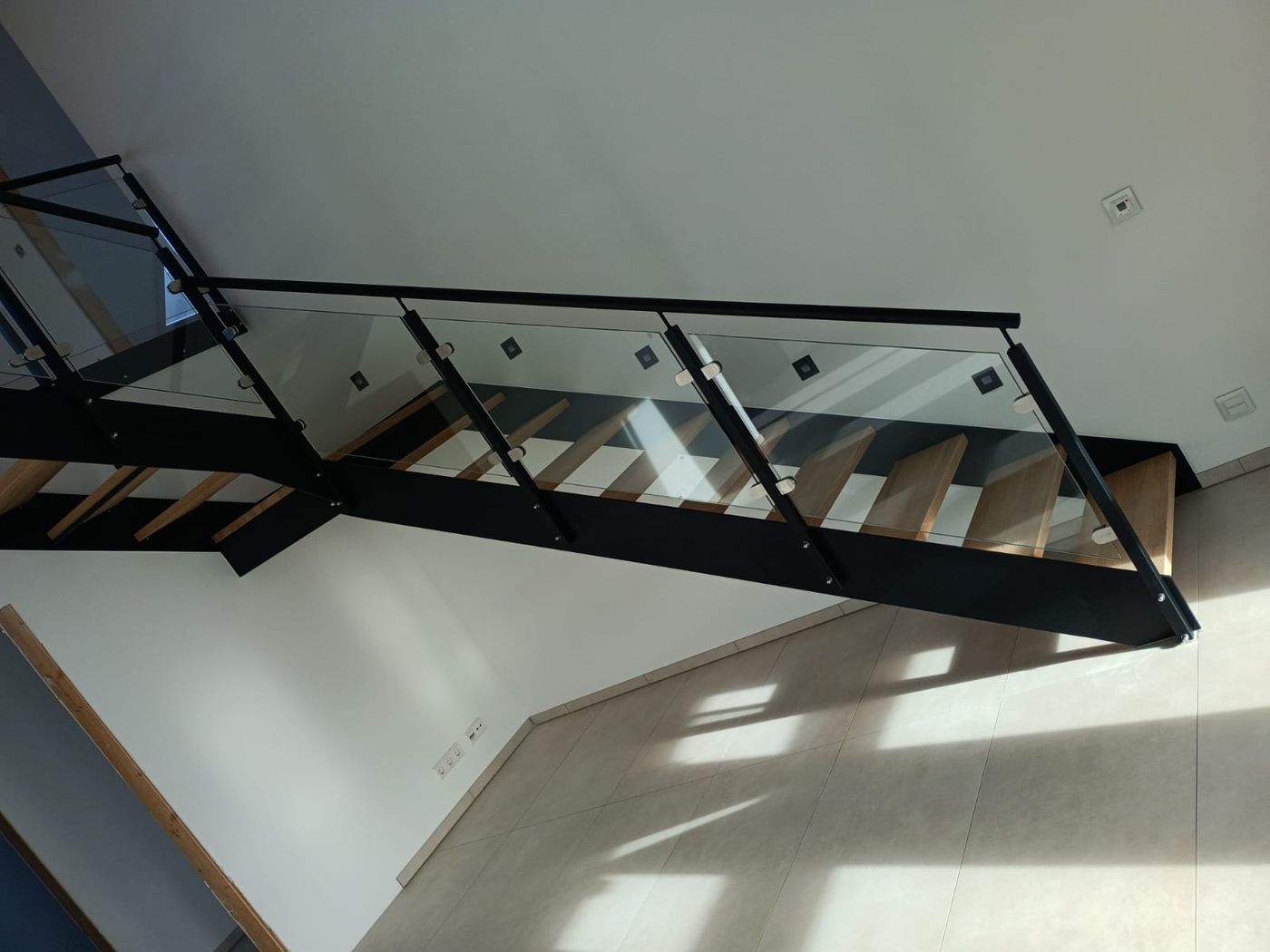 Untersicht einer schwarzen Treppenkonstruktion mit Holzstufen und Glasgeländer.