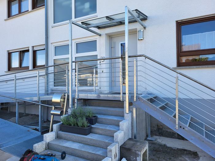 Vordach mit transparenter Deckung über einer Eingangstreppe mit Metallgeländer.