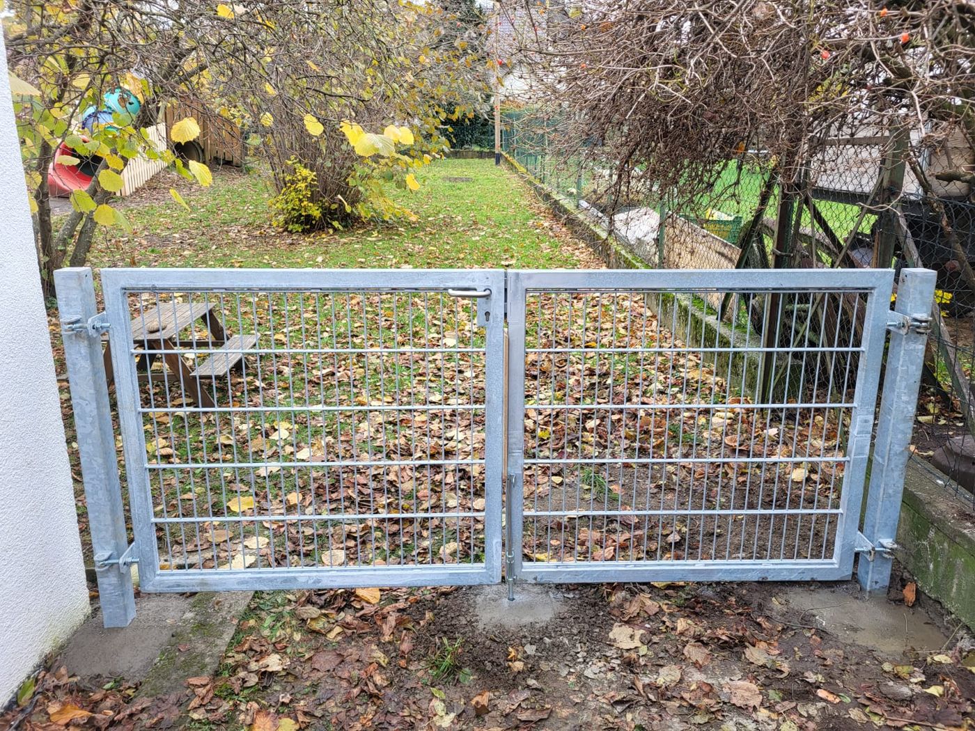 Frontansicht eines zweiflügeligen Metalltores mit Gitterfüllung vor einem Garten.