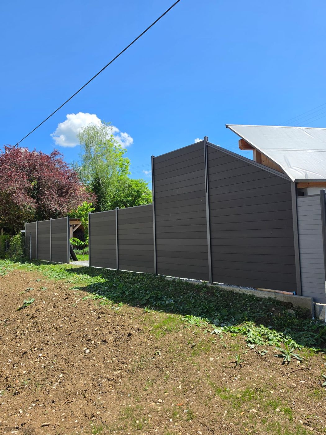 Hohe dunkle Sichtschutzwand mit waagerechten Lamellen im Garten.